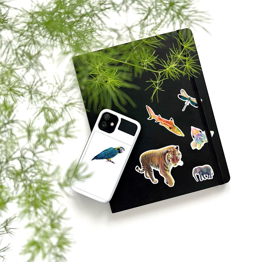 parrot, tiger, shark, dragonfly, fish, and elephant vinyl stickers on phone and notebook
